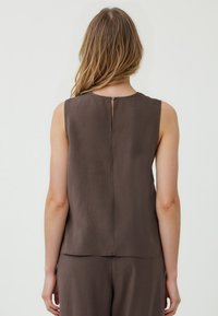 Top marrone senza maniche con scollatura rotonda e un piccolo spacco posteriore fissato con un bottone, realizzato in tessuto morbido e leggero.