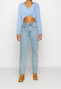 Jasnoniebieska, przycięta bluzka z długim rękawem i dekoltem w serek, z kręconym przodem, zestawiona z jasnoniebieskimi spodniami z wysokim stanem i prostymi nogawkami oraz beżowymi botkami na słupku.