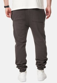 Dunkelgraue Jogginghosen mit lockerer Passform, elastischen Bündchen und zwei Gesäßtaschen, kombiniert mit weißen Sneakern. Glatte Textur und lässiges Design.