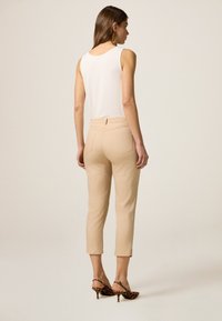 Beige cropped broek met een gladde textuur, ontworpen met een hoge tailleband en twee achterzakken, gecombineerd met een wit mouwloos topje.