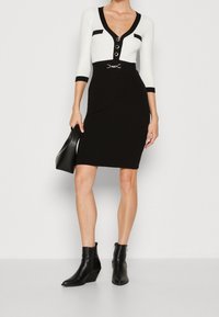 Svart och vit figursydd klänning med V-hals, trekvartslånga ärmar och bältesaccent. Bärs med svart stövlar i ankelhöjd och en handväska.