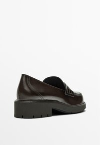 Black patent leather loafers with a chunky heel and textured detailing on the upper. Flat, ridged sole for added grip.