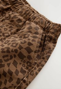 Brązowa tkanina w leoparda o miękkiej teksturze, z elastycznym pasem w talii i detalami bocznych kieszeni, prezentująca wyraźny wzór.