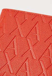 Red textured wallet with embossed geometric patterns, featuring a smooth finish and contrasting stitching along the edges.