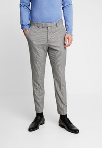 Pantaloni grigi e neri con motivo a righe, dalla vestibilità affusolata, dotati di tasche e parte frontale piatta. Indossati con una maglietta a maniche lunghe blu chiaro e scarpe nere.