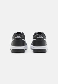Fekete-fehér sportcipők, bőrből készült felsőrésszel, párnázott nyakkal és texturált gumitalppal. A sarokon "new balance" felirat található.