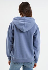 Felpa con cappuccio blu dal fit rilassato, con polsini e orlo a coste. Tessuto morbido, schiena senza dettagli e un grande cappuccio. Abbinata a jeans di denim.