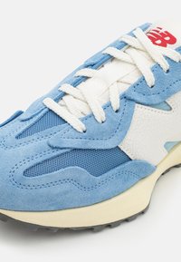 Modré semišové a síťované tenisky s bílou boční panelem, krémovou mezipodešví a šedou gumovou podrážkou s texturovaným detailem.