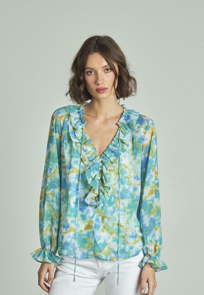 Leichte Bluse in Blau und Grün mit einem Batikmuster, gerafftem Ausschnitt, Knöpfen und weit ausgestellten Ärmeln. Glatter Stoff mit leichtem Glanz.