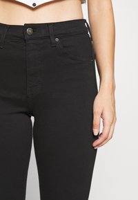 Svarta högmidjade jeans gjorda av elastisk denim med en slät yta, femficksdesign och knappknäppning fram.
