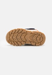 Podeszwa buta o wytrzymałej konstrukcji; posiada jasnobrązową gumową teksturę z głębokimi wzorami bieżnika zapewniającymi przyczepność i trwałość.