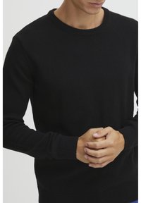 Black crew-neck sweater made of textured fabric. Features ribbed cuffs and hem, fitted design, and long sleeves.