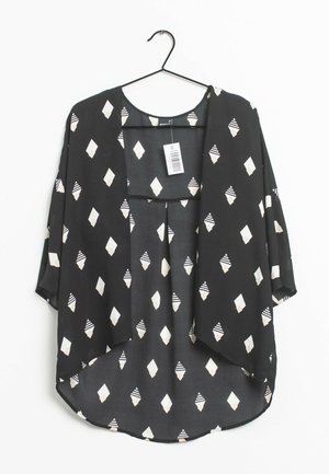 Czarna luźna bluzka z białymi wzorami w kształcie diamentów, zawieszona na czarnym wieszaku, z okrągłym dekoltem i metką przymocowaną przy kołnierzu.