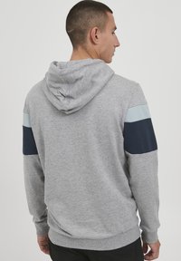 Grå hettegenser med snorhette, med lys blå og marineblå ermeakenter. Myk stoff, avslappet passform og ribbestrikkede mansjetter.