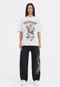 Overmaat wit T-shirt met een kleurrijk ontwerp van een schedel en een slang, gecombineerd met zwarte broek met kleurrijke draakborduursel.