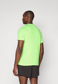 Neon green athletic t-shirt with short sleeves, round neckline, and smooth texture, paired with dark shorts, viewed from the back.