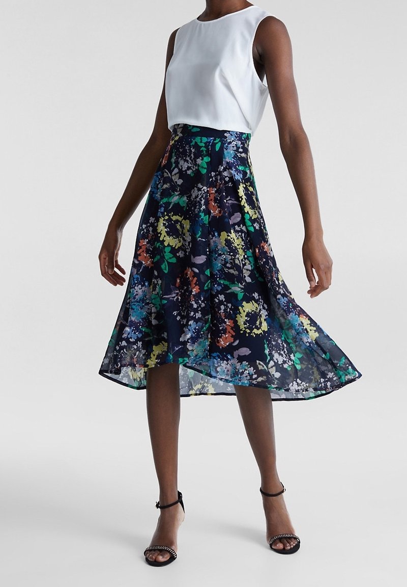 Blommig midi kjol med marinblå bakgrund, färgglad blommönster; tillsammans med en vit ärmlös topp. Slätt tyg med en flödande form.