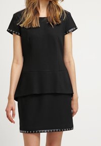 Musta peplum-mekko lyhyillä hihoilla, hopeiset napit hihojen cuffsissa ja helmassa, valmistettu sileästä kankaasta. Rakenne on huolellisesti suunniteltu.