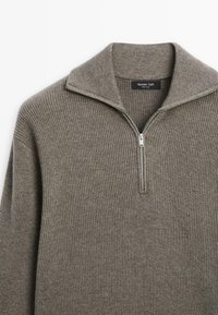 Grauer gerippter Pullover mit hohem Kragen und halbem Reißverschluss. Weiche Textur und schlichtes Design ohne zusätzliche Verzierungen.