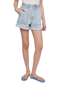 Shorts in denim azzurro con vita alta, orli arrotolati e tasche laterali. Abbinati a sandali blu con una delicata catenina alla caviglia.