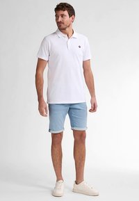 Hvid polo med en lille logo på brystet, kombineret med lyseblå denimshorts rullet op og hvide sneakers. Casual design og pasform.