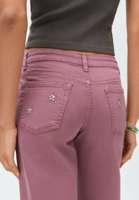 Vaqueros rosas con una textura suave, con bordados en forma de estrella en los bolsillos traseros. Cintura de altura media y corte ajustado.