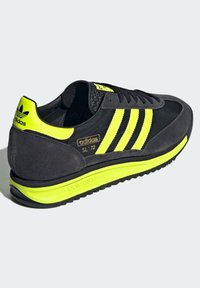 Tenisky Adidas SL '72 mají černý svršek z semiše a textilu s fluorescenčně žlutými akcenty, třemi pruhy a texturovanou gumovou podrážkou.