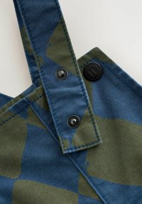 Salopete din denim cu un model de camuflaj albastru și verde, bretele ajustabile și accesorii cu nasturi negri. Accente cusute vizibile.