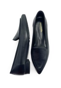 Bailarinas de cuero negro con puntera puntiaguda, tacón plano, ribete elástico y textura lisa. Marca dorada en la plantilla.