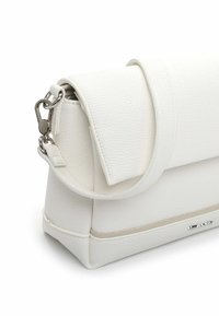 Balta ādas rokassoma ar teksturētu virsmu, pārklājamu atloku un sudraba metāla aizdari. Ar izliekta roktura un smalku šuvju dizainu.