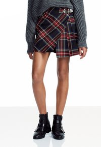 Zwarte geruite rok met rode, blauwe en witte accenten, met een wikkelontwerp en riemdetail. Draag het met zwarte, gebuckle enkellaarzen.