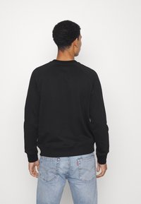 Sudadera negra de cuello redondo, con puños y dobladillo acanalados, fabricada con tela suave. Combinada con jeans de mezclilla azul claro. El fondo es blanco liso.