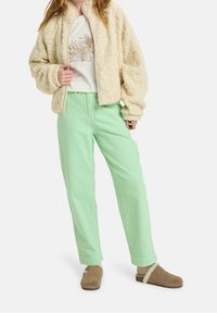 Beżowa, teksturowana kurtka na zamek, biały t-shirt z kwiatowym nadrukiem, luźne spodnie w kolorze mięty oraz brązowe wsuwane buty z futrzanym ociepleniem.