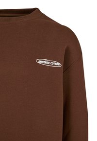 Sudadera marrón de algodón, con un cuello redondo y mangas largas. Incluye el logo blanco "ANOTHER COTTON" en el pecho.