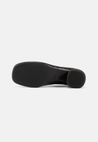 Încălțăminte neagră cu o suprafață inferioară netedă, având un model texturat și un toc rotunjit. Designul este minimalist și aerodinamic.