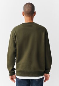 Olivgrön sweatshirt med rund hals, ribbade muddar och fåll, mjuk textur och avslappnad passform. Bakifrån, med minimalistiska designdetaljer.
