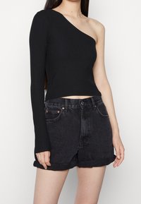 Schwarzes geripptes Oberteil mit einem langen Ärmel und einer exponierten Schulter, kombiniert mit schwarzen Denim-Shorts mit umgeschlagenem Saum und einem Knopfverschluss.