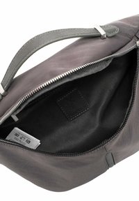 Harmaa nahkalaukku, jossa sileä pinta, yläsalpaketju ja yksinkertainen kahva. Sisäpuolella musta kangasvuori ja etikettejä.