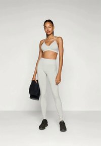 Ensemble de sport gris clair comprenant un bralette à fines bretelles et un legging taille haute. Texture lisse, complétée par des baskets noires.
