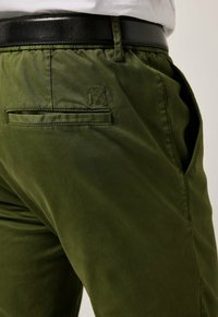 Olijf groene broek van gladde stof, met een achterzak, elastische tailleband en een zwarte riem met een strakke afwerking.