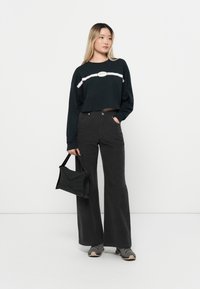 Sweatshirt noir court avec une bande blanche et un logo, associé à un pantalon noir évasé taille haute et un sac à main noir. Les baskets sont grises.