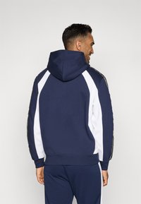 Sweatshirt com capuz em azul-marinho com mangas brancas, apresentando costuras contrastantes e um acabamento texturizado. A bainha e as mangas ribadas realçam o design.