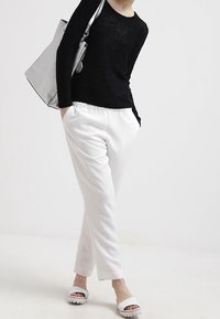 Schwarz strukturierter Strickpullover, weiße maßgeschneiderte Hosen und weiße Slide-Sandalen. Silbertote-Tasche mit einfachem Design.