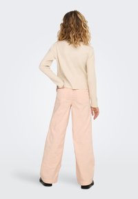 Beige ribbed sweater, cropped design, paired with light pink wide-legged pants featuring back pockets. Black shoes complete the outfit.
