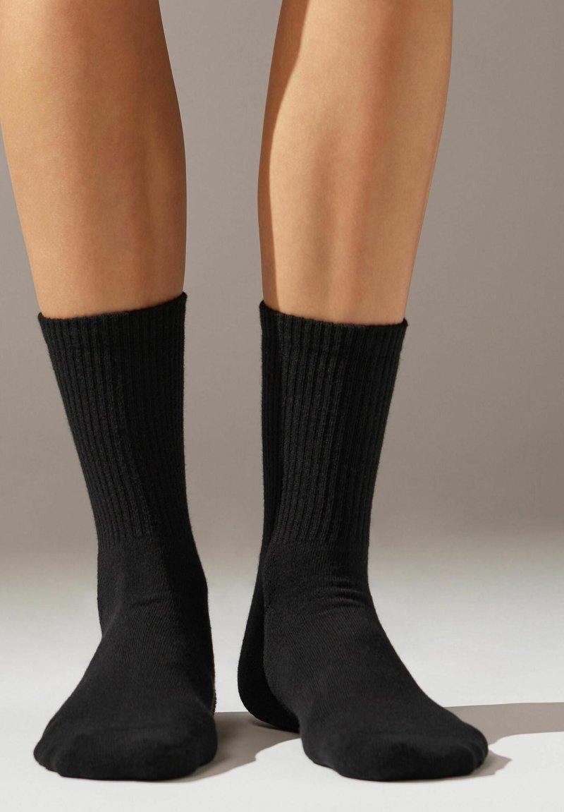 Calcetines de algodón negros con textura acanalada, de longitud hasta la mitad de la pantorrilla y puntera y talón reforzados para mayor durabilidad. Diseño sencillo sin patrones.