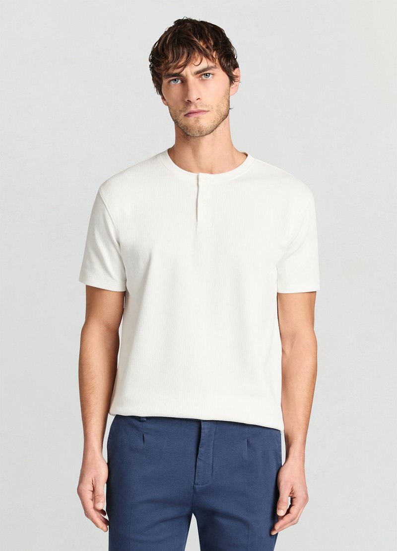 Weißes, geripptes Henley-T-Shirt mit kurzen Ärmeln, rundem Ausschnitt und einem Knopfverschluss, kombiniert mit einer marineblauen Hose.