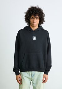 Black hoodie made of soft material with a kangaroo pocket, featuring a small grey logo on the chest. Smooth texture and relaxed fit.