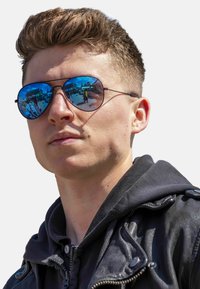 Sunglasses with mirrored blue lenses in round shape, thin black metal frame, worn with a black leather jacket and hoodie.