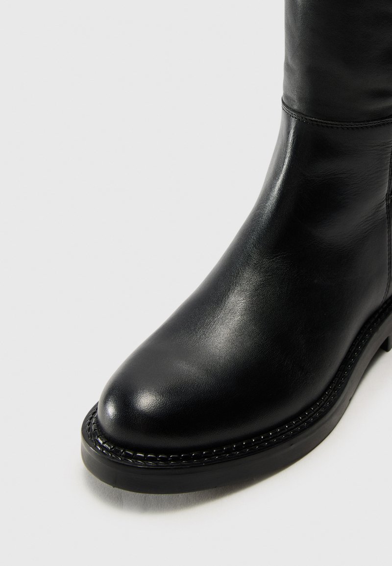 Czarne skórzane botki za kostkę z zaokrąglonym noskiem, gładką fakturą i dekoracyjnym przeszyciem wzdłuż podeszwy. Posiadają niską, solidną obcas.
