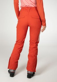 Pantalons de ski rouges avec une taille haute, des poches zippées sur les côtés et des zips aux ouvertures des jambes. Fabriqués à partir d'un matériau synthétique à la texture lisse.